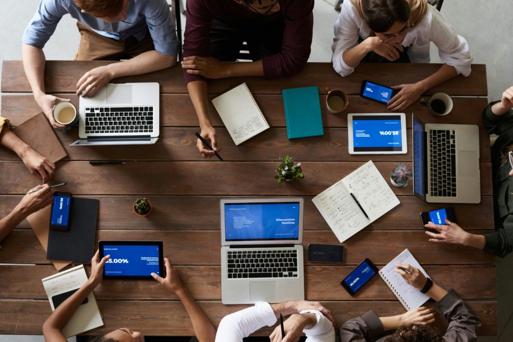 A group of people sitting around a desk with only their arms and devices showing